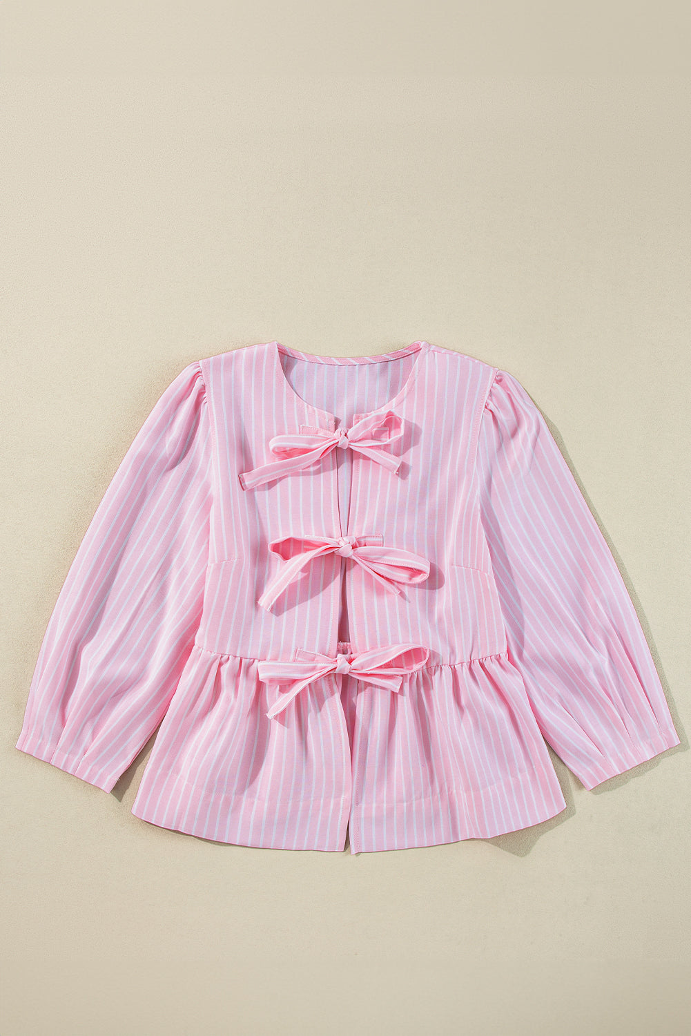 Blush pink striped peplum blouse with three bow details and long sleeves.