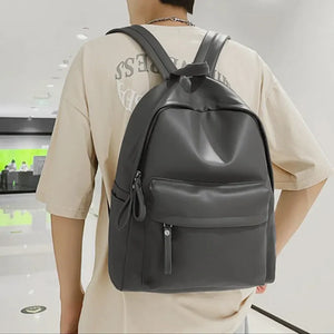Dark gray minimalist leather backpack with front pocket and zipper details.