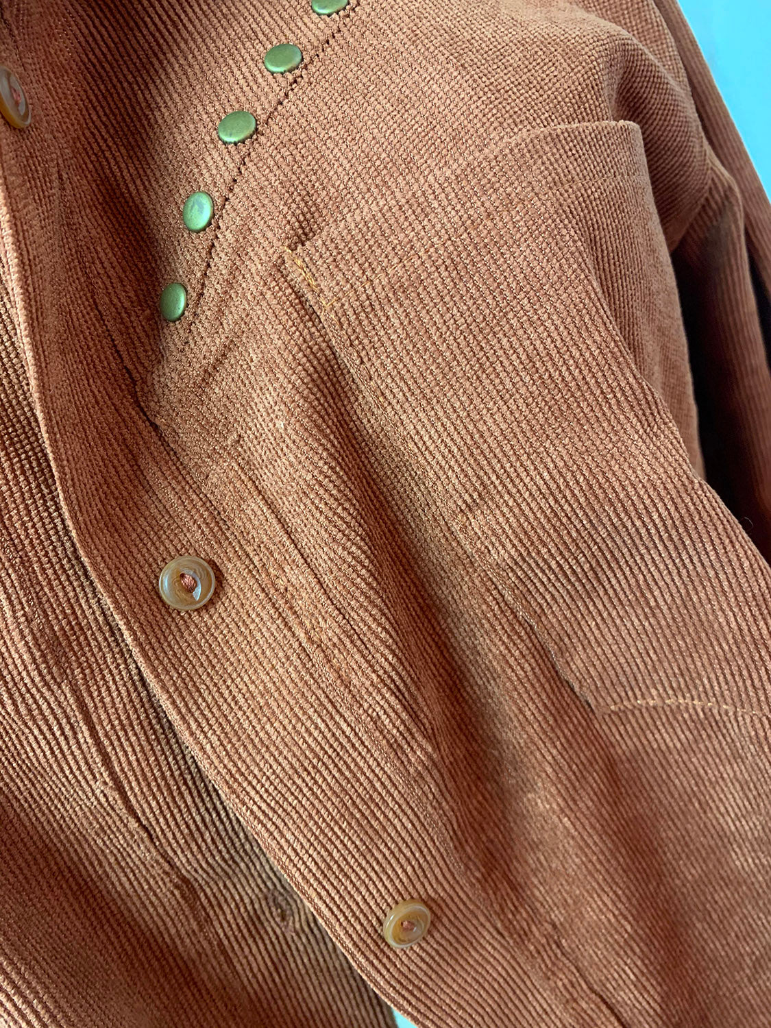 Brown corduroy shirt jacket with green studded buttons and chest pocket detail.
