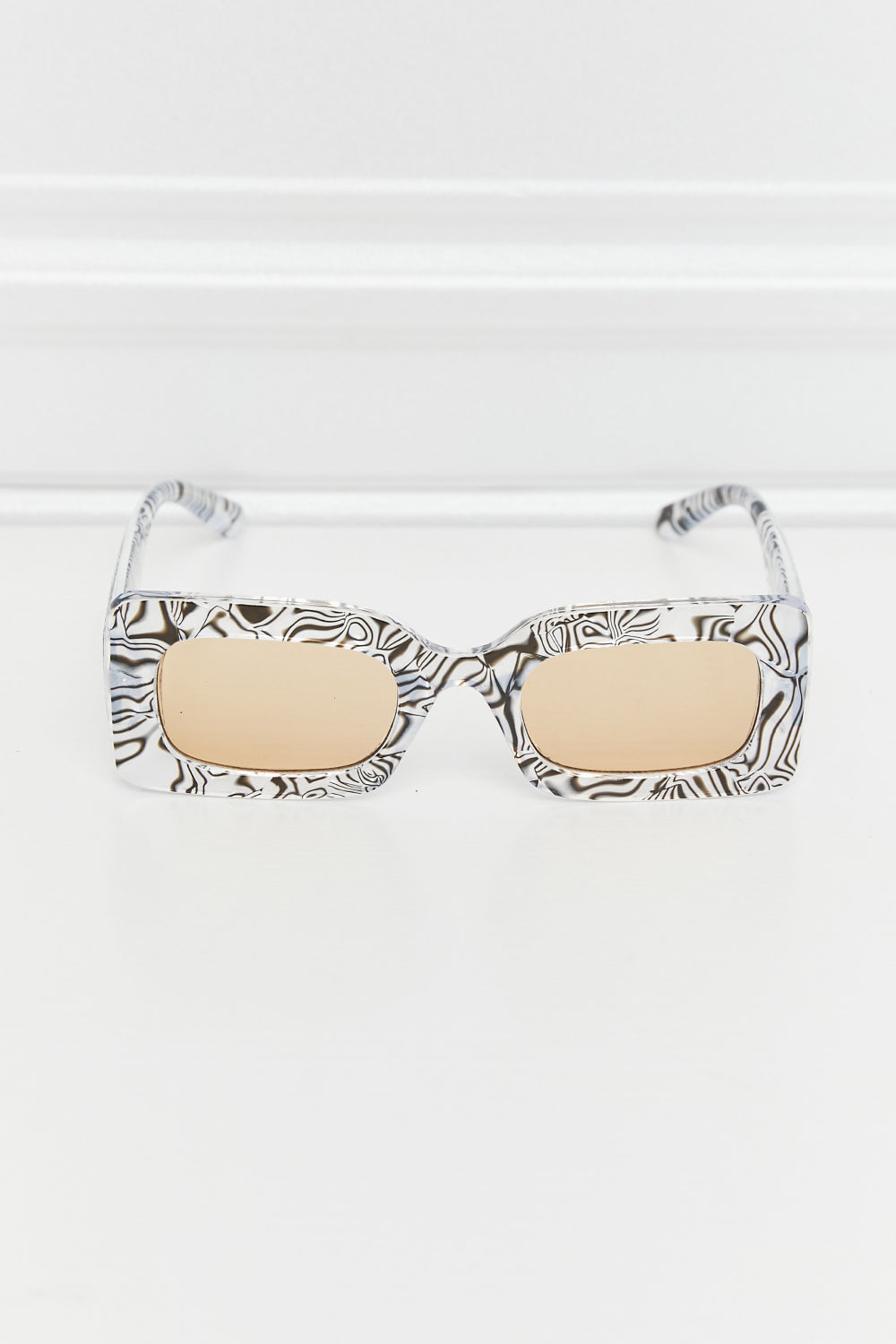 Swirl print rectangular frame sunglasses with tan lenses and black and white pattern.
