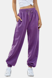 Purple sweatpants with gathered cuffs and drawstring waist, styled with white sneakers.