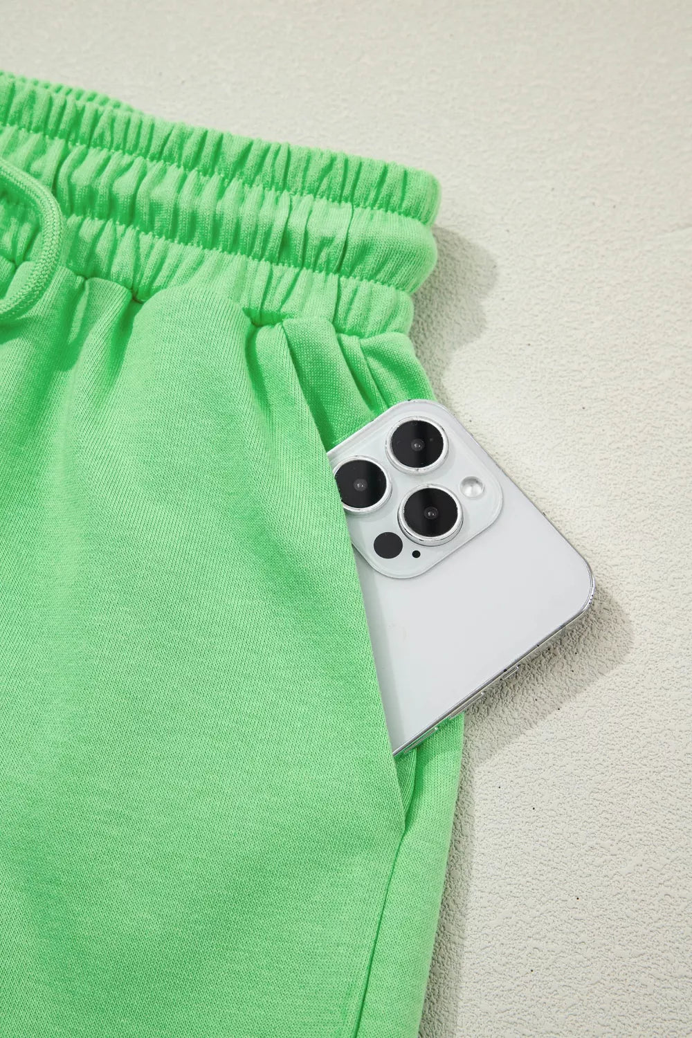 Green cotton drawstring shorts with elastic waist and pocket detail, phone shown.