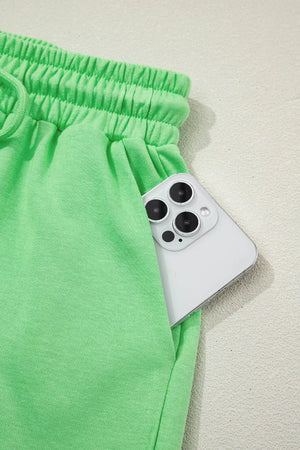 Green cotton drawstring shorts with elastic waist and pocket detail, phone shown.