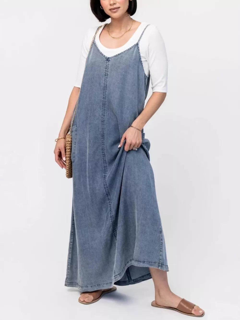 Light blue denim maxi dress with V-neck and adjustable straps, worn over a white tee.