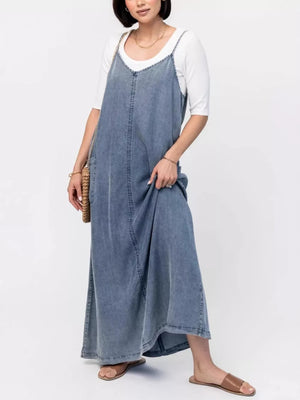 Light blue denim maxi dress with V-neck and adjustable straps, worn over a white tee.
