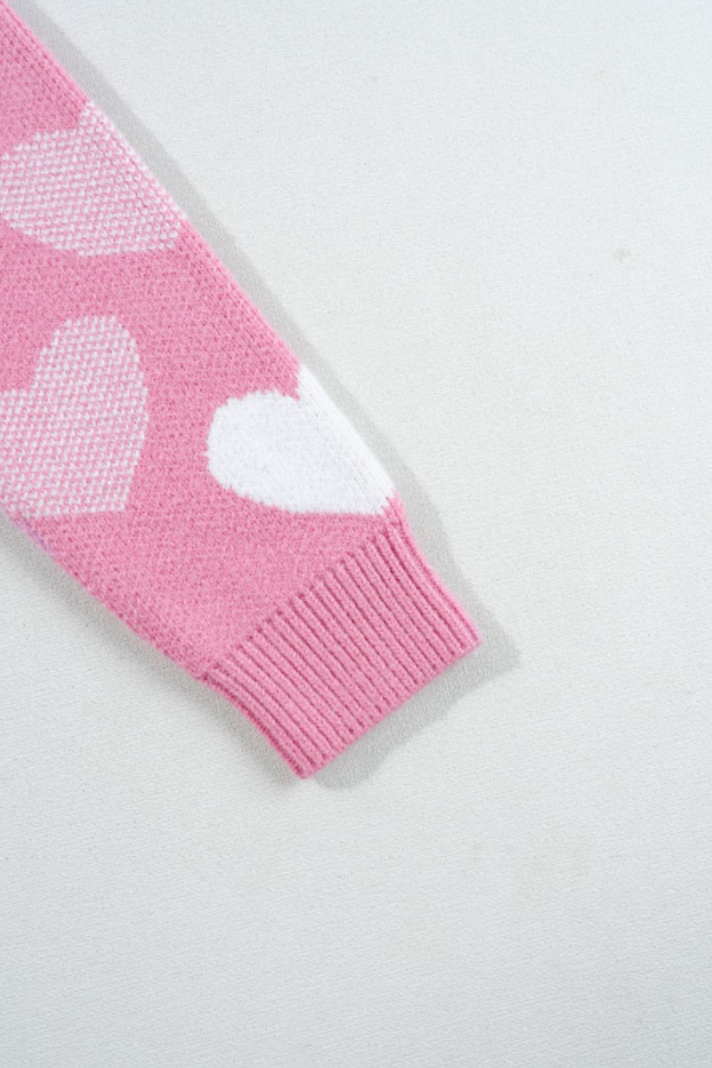 Pink knit sweater with white heart intarsia pattern and ribbed cuff detail.