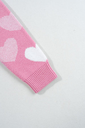 Pink knit sweater with white heart intarsia pattern and ribbed cuff detail.