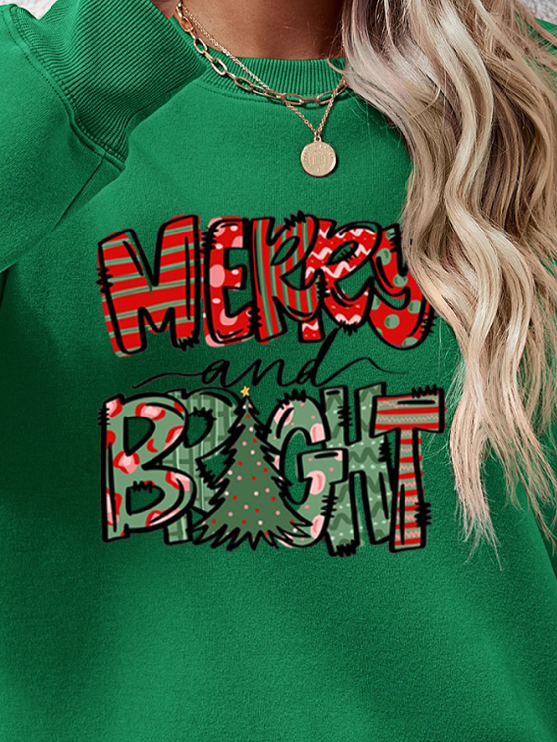 Green crewneck sweatshirt with Merry and Bright Christmas graphic and festive tree detail.