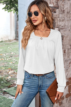White long sleeve top with square neckline and subtle pleats, styled with jeans.
