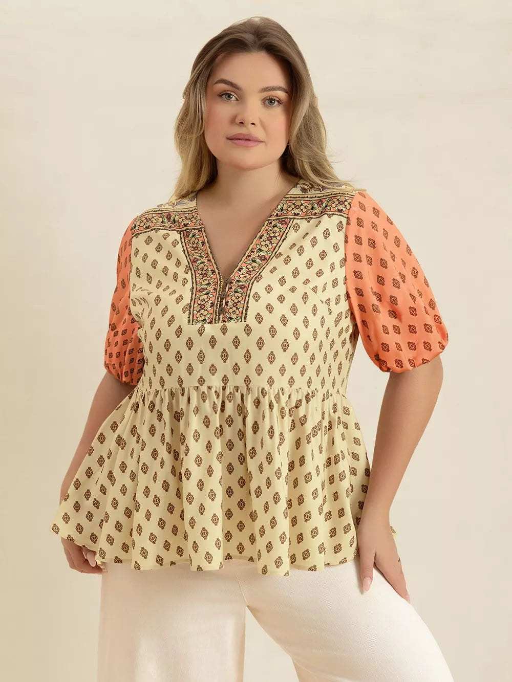 Vibrant geometric peplum shirt with coral sleeves and v-neckline.