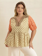 Vibrant geometric peplum shirt with coral sleeves and v-neckline.