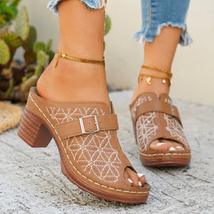 Tan buckle sandals with white floral embroidery and a block heel.