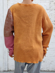 Colorblock knit sweater in sherbet orange with contrasting sleeves and button cuff detail.