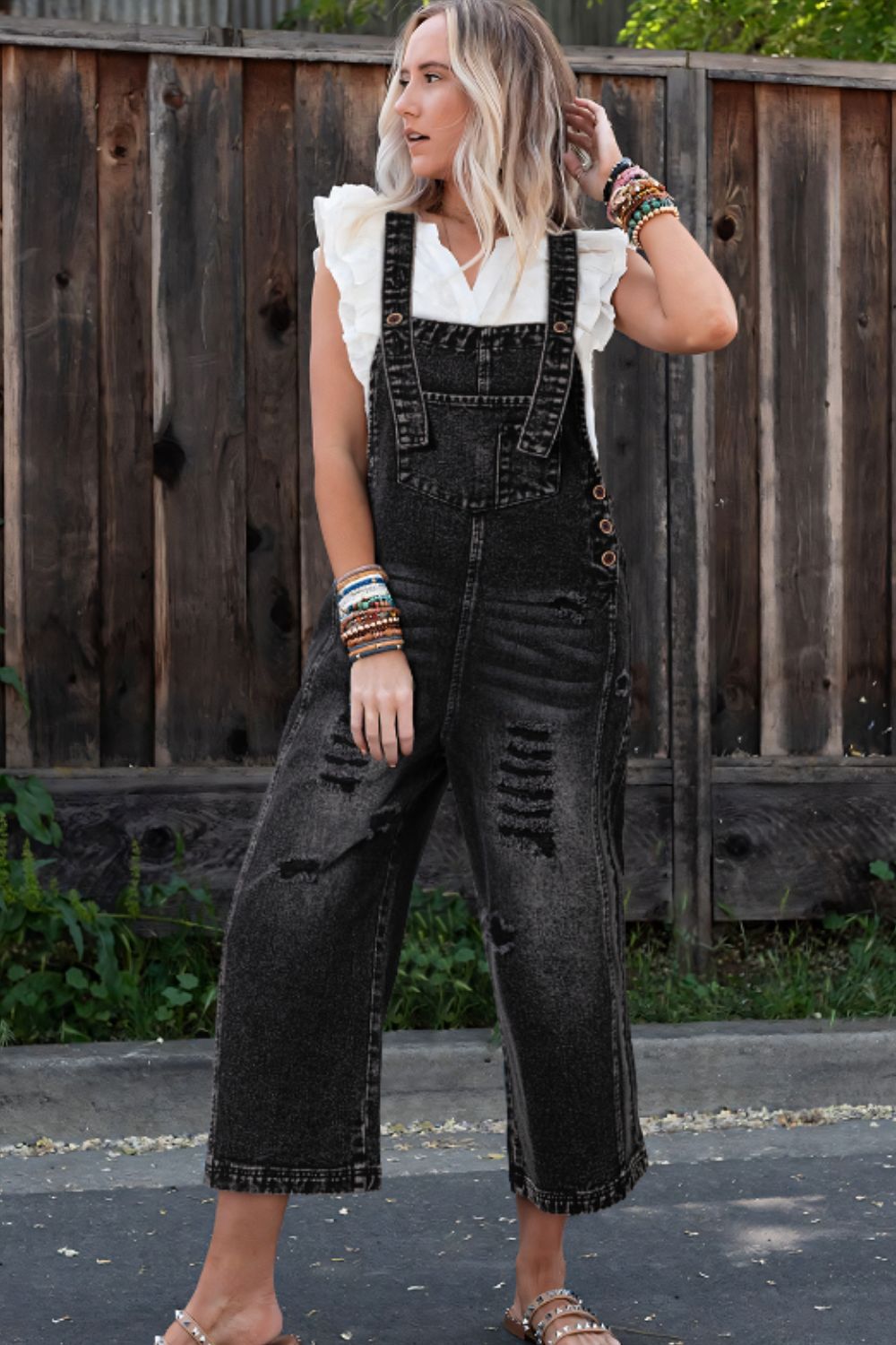 Black distressed denim culotte overalls with a cropped wide leg and button side closures.