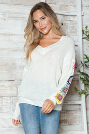 White knit sweater with colorful granny square crochet sleeves and V-neck.