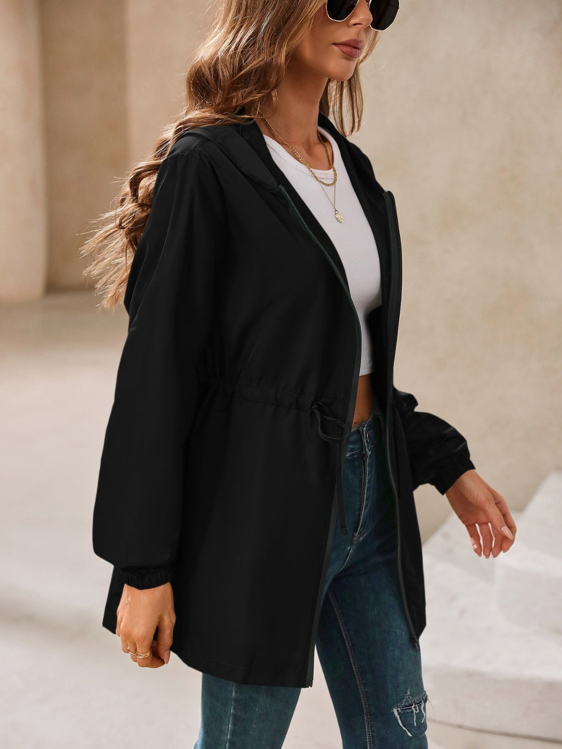 Black hooded jacket with cinched waistline and zip front, styled with jeans.