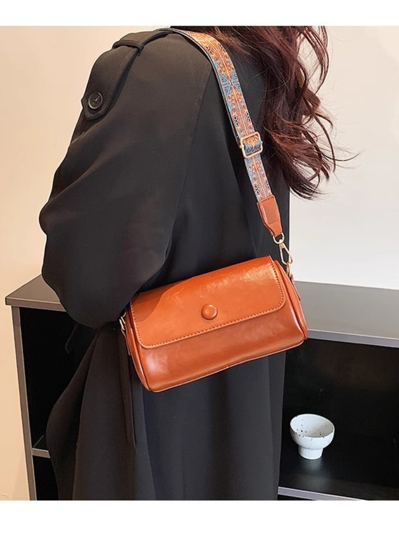 Brown leather crossbody bag with adjustable ethnic strap and button closure.