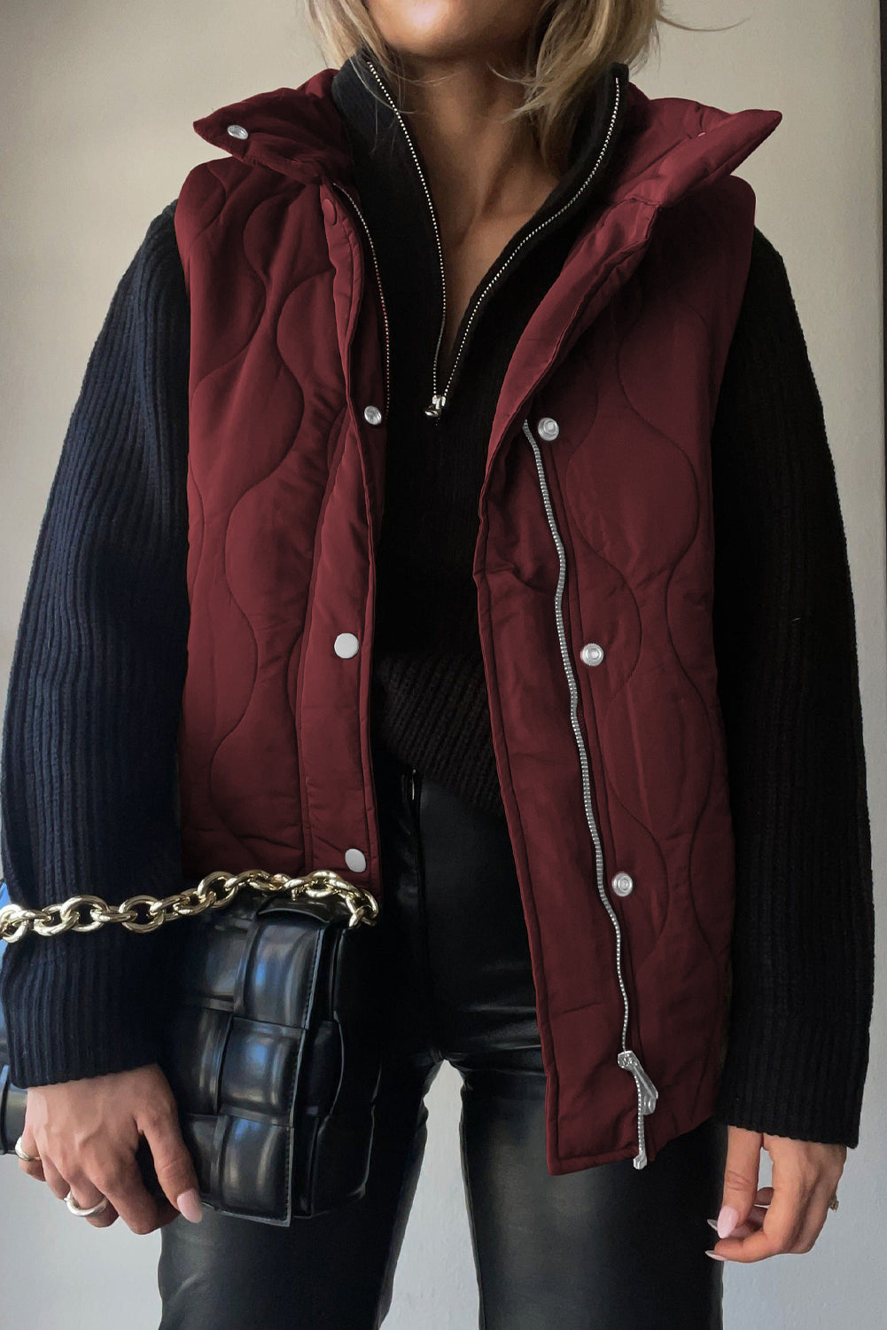 Wine quilted stand-collar utility gilet with silver zipper and snap closures, worn over a black sweater.