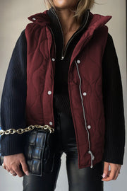 Wine quilted stand-collar utility gilet with silver zipper and snap closures, worn over a black sweater.