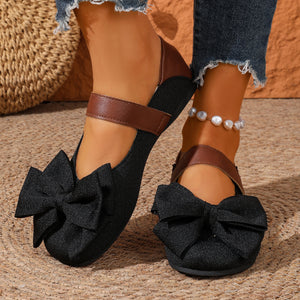 Black round toe flats with textured fabric and large bow detail, featuring a brown strap.