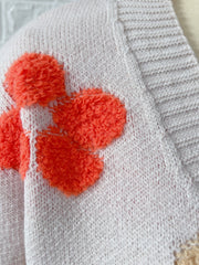 White knit cardigan with textured orange floral appliqués and ribbed trim.