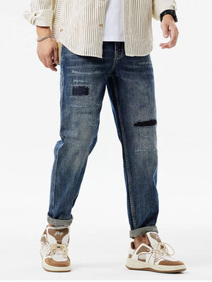 Men's dark blue distressed cotton jeans with patchwork details and cuffed hems.