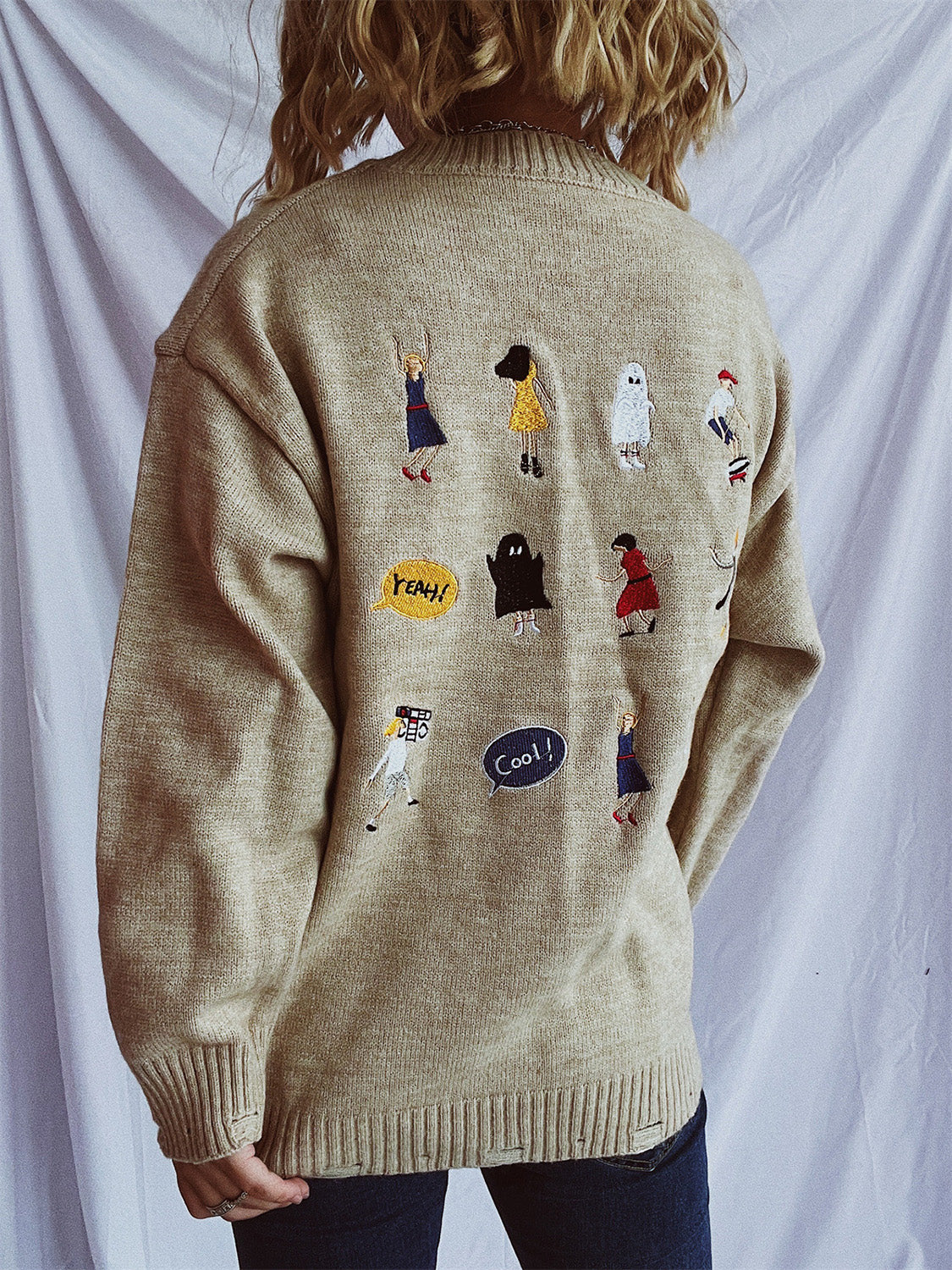 Tan relaxed knit sweater with embroidered characters and speech bubbles on the back.