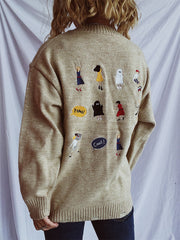 Tan relaxed knit sweater with embroidered characters and speech bubbles on the back.