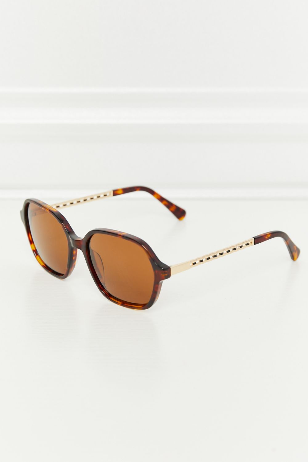 Tortoiseshell hexagonal frame sunglasses with gold accent temples and brown lenses.