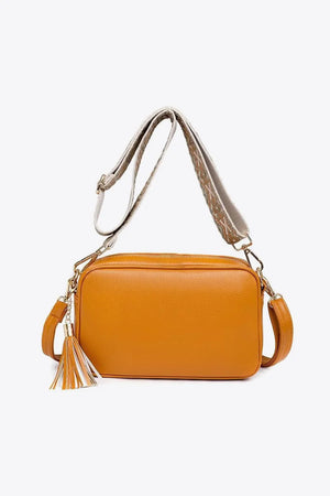 Orange textured crossbody bag with tassel detail and patterned strap