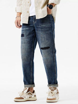 Men's dark blue distressed denim jeans with patchwork details and cuffed hems.