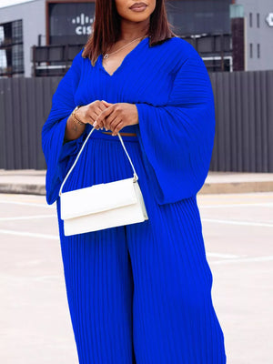 Blue pleated two-piece set with V-neck top and wide-leg pants, styled with a white clutch.