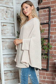 Cream knit sweater with cape sleeves and v-neck, styled with distressed jeans.