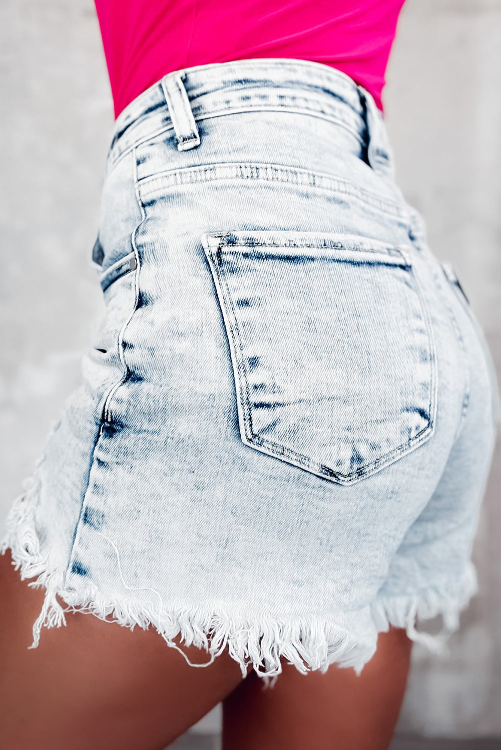 Light wash denim shorts with frayed hem and asymmetric waistband detail.