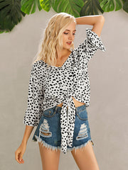Spotted knot-front blouse with flared sleeves and button detail, styled with denim shorts.