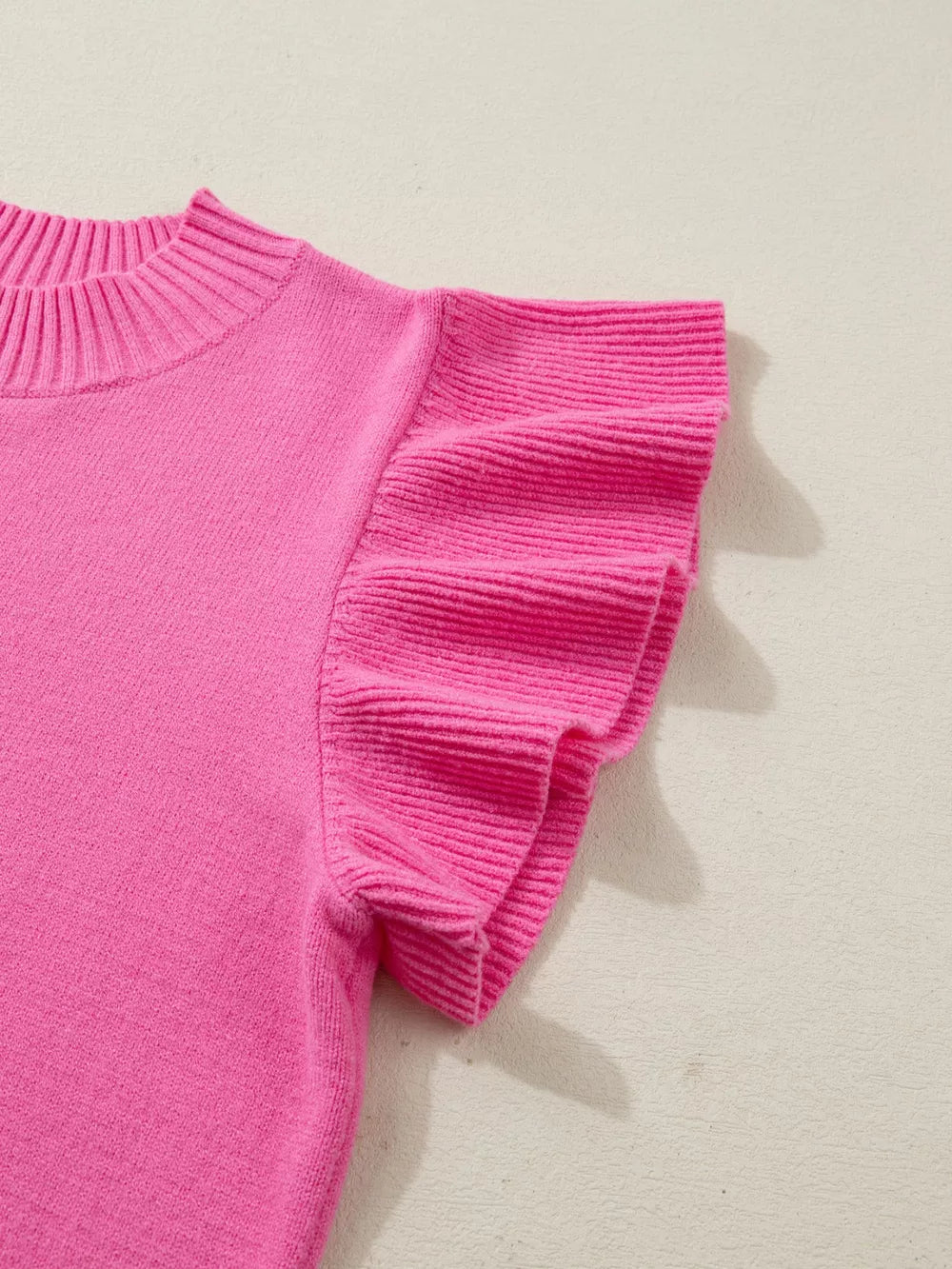 Pink knit top with ruffled short sleeves and ribbed mock neck.