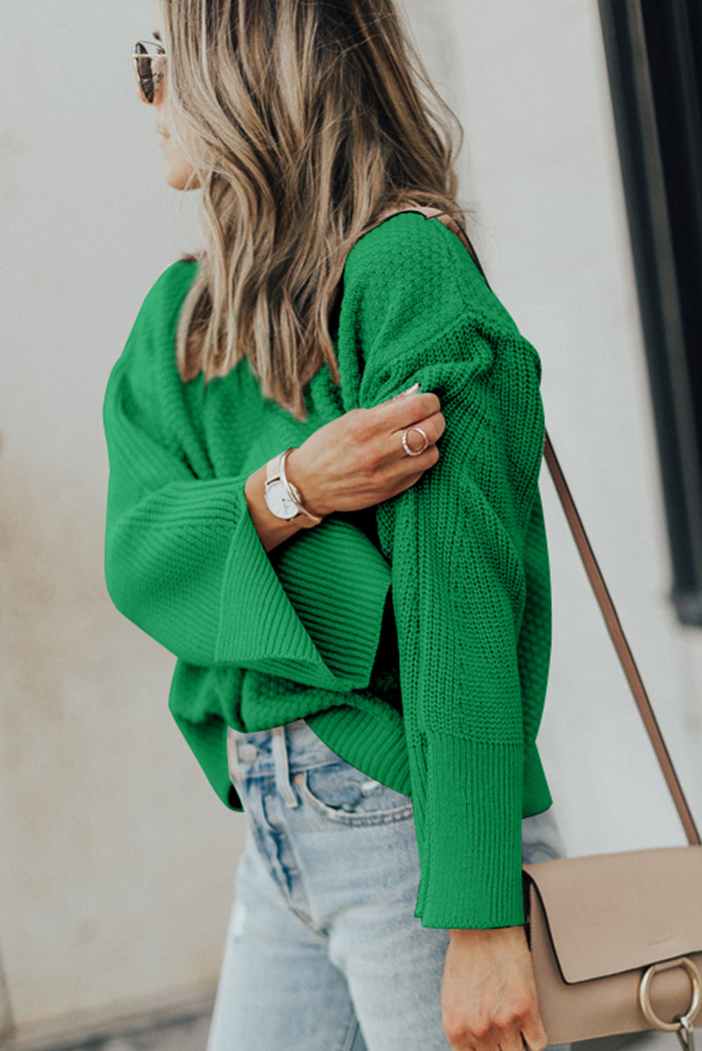 Green knit sweater with textured sleeves and side slits, styled with jeans.