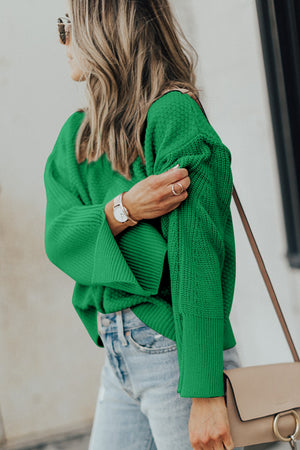 Green knit sweater with textured sleeves and side slits, styled with jeans.