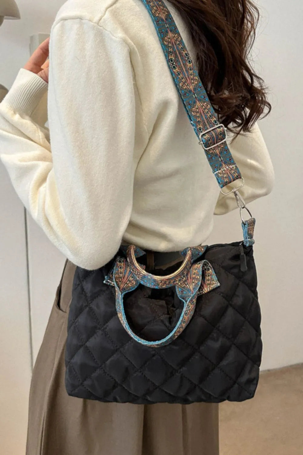 Black quilted satchel bag with ornate patterned strap and handles.