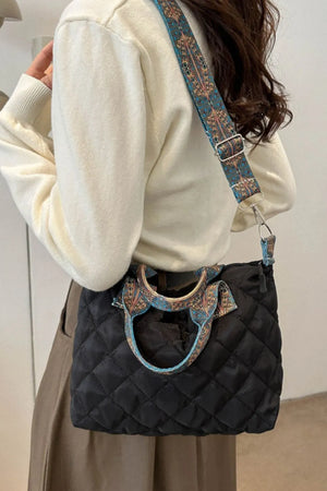 Black quilted satchel bag with ornate patterned strap and handles.