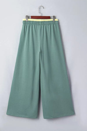 Green cotton sweatpants with wide legs and a yellow drawstring waistband.