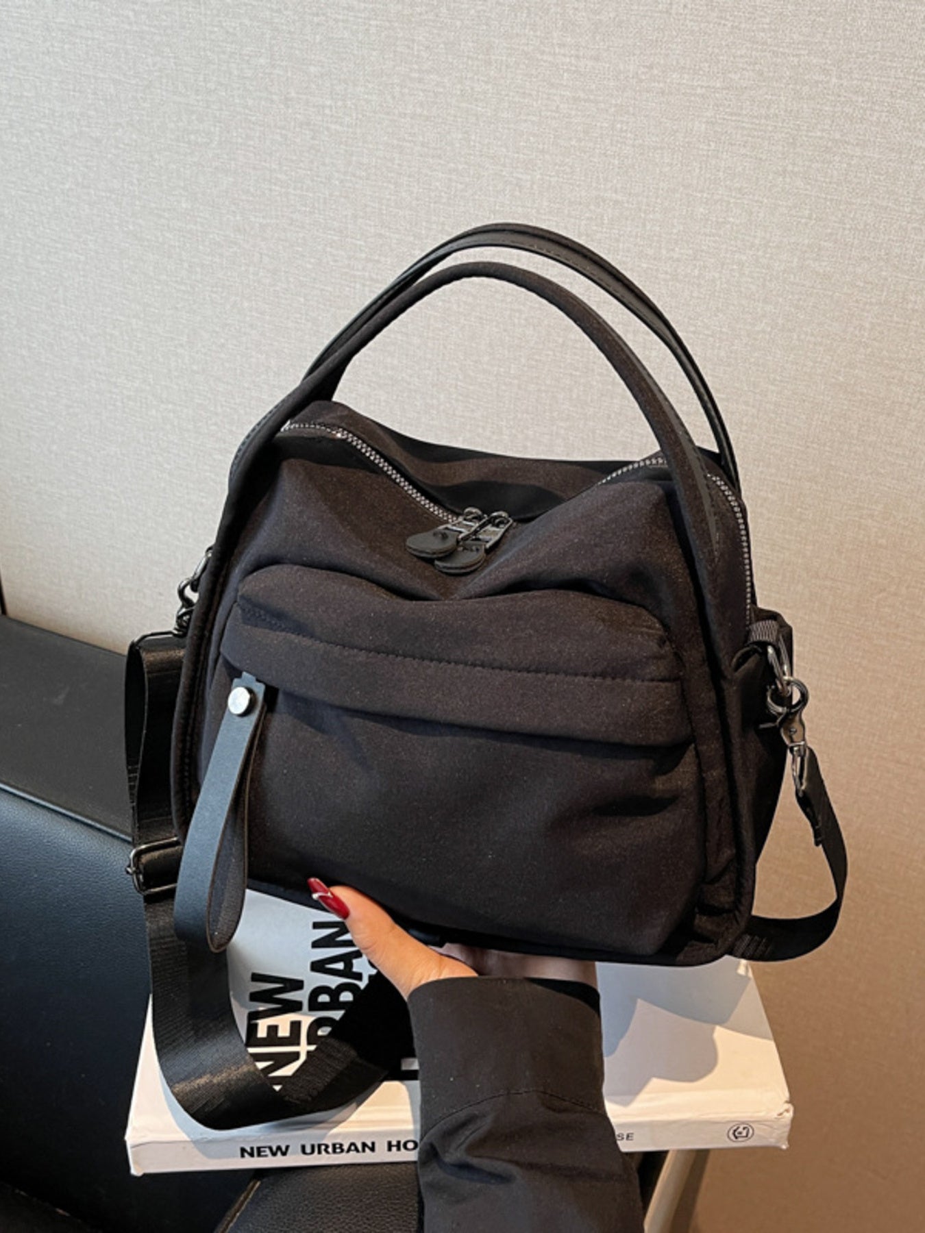 Black crossbody bag with decorative pull tab and dual zippers.