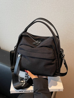 Black crossbody bag with decorative pull tab and dual zippers.
