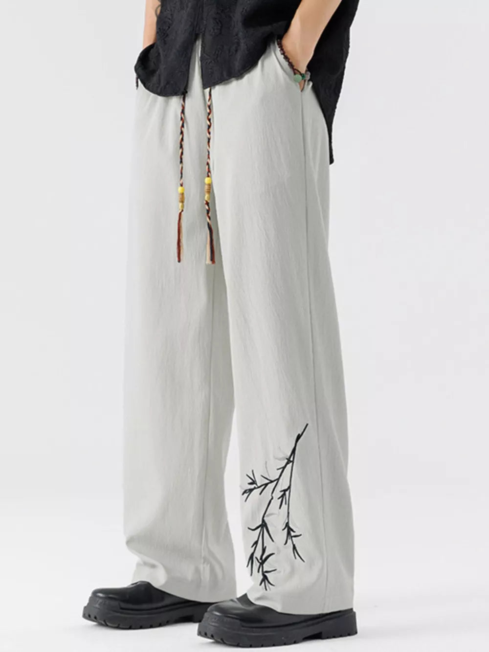 Light gray wide-leg sweatpants with black branch embroidery and braided drawstring.