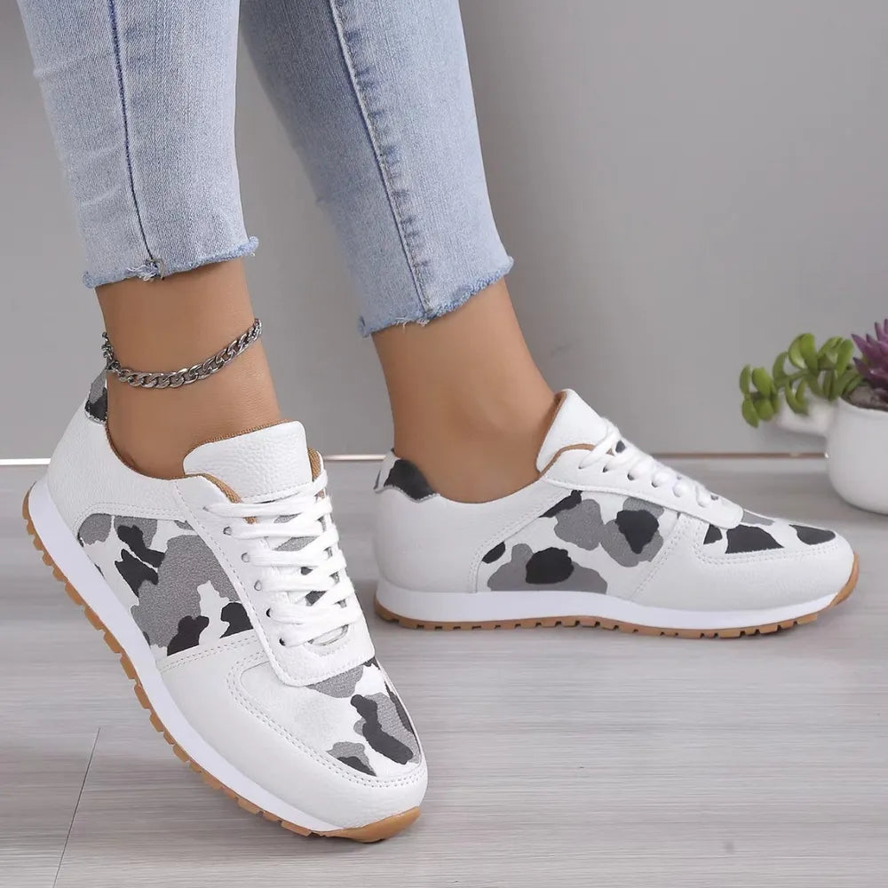 White sneakers with black and grey camouflage print panels and gum soles.