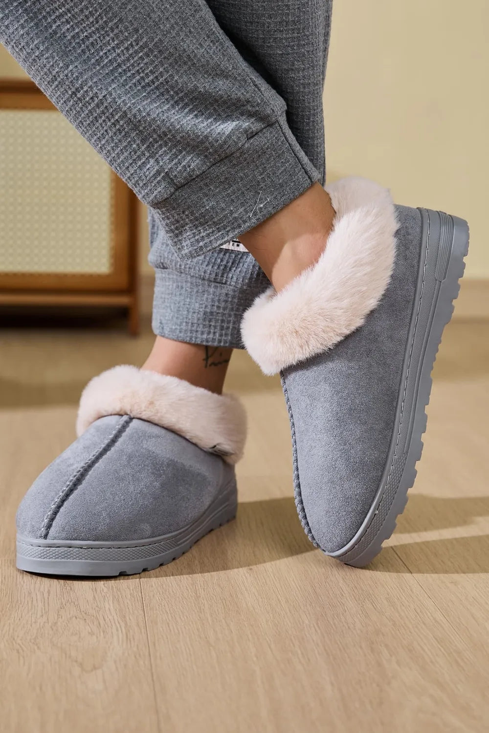 Gray suede slippers with plush shearling trim and stitched detail.