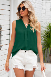 Green textured sleeveless V-neck blouse with front pleats, styled with white shorts.