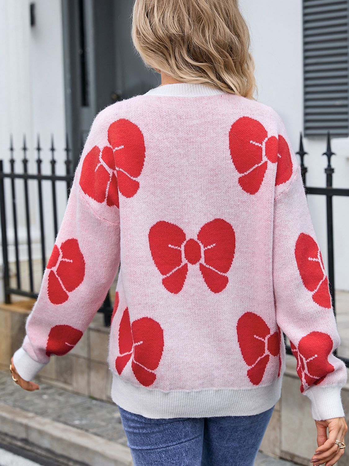 Pink knit sweater with allover red bow pattern, crew neck, long sleeves.