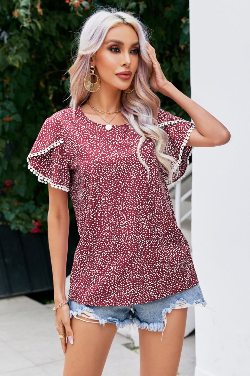 Burgundy dotted blouse with flutter sleeves and pom-pom trim.
