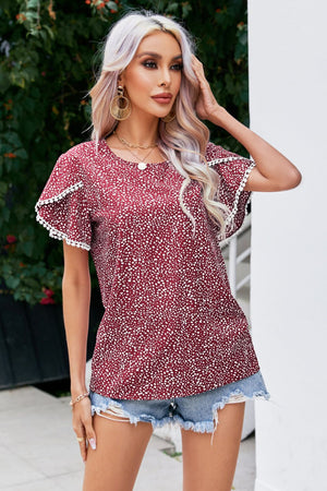 Burgundy dotted blouse with flutter sleeves and pom-pom trim.